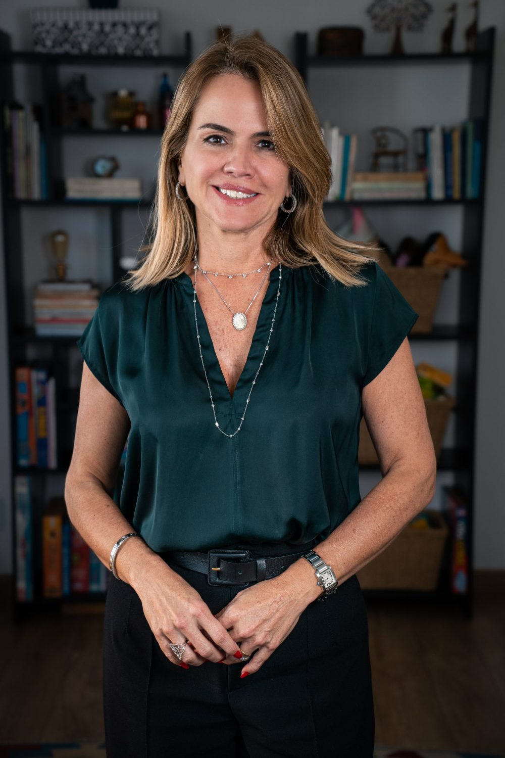 Lecticia Raposo em pé diante da estante de livros do consultório, sorrindo