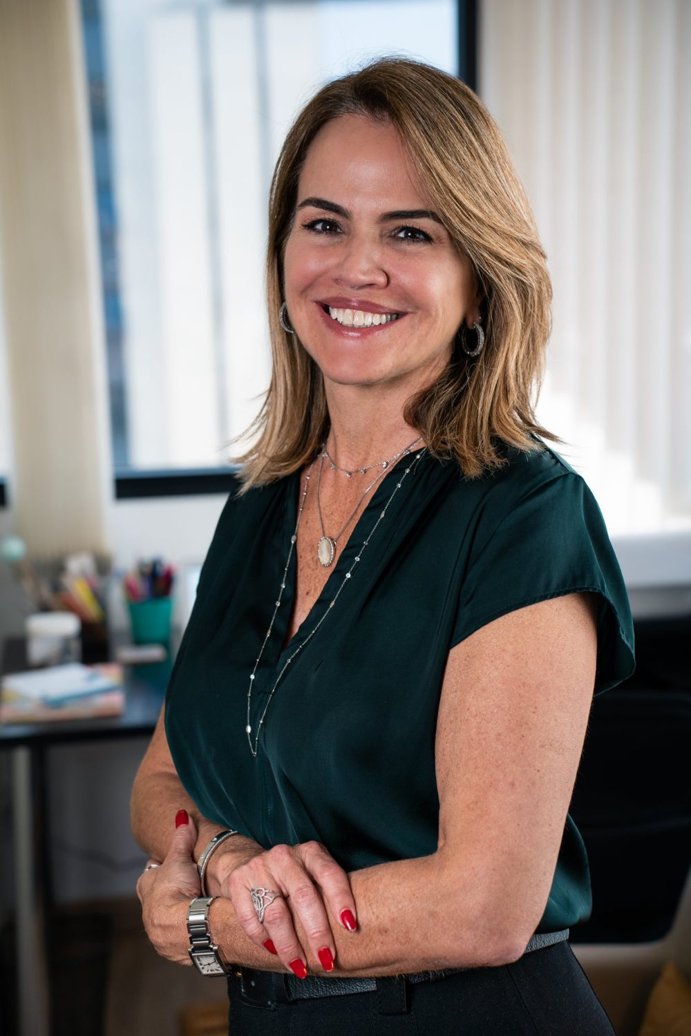 Lecticia Raposo sorrindo, de braços cruzados, junto à janela do consultório